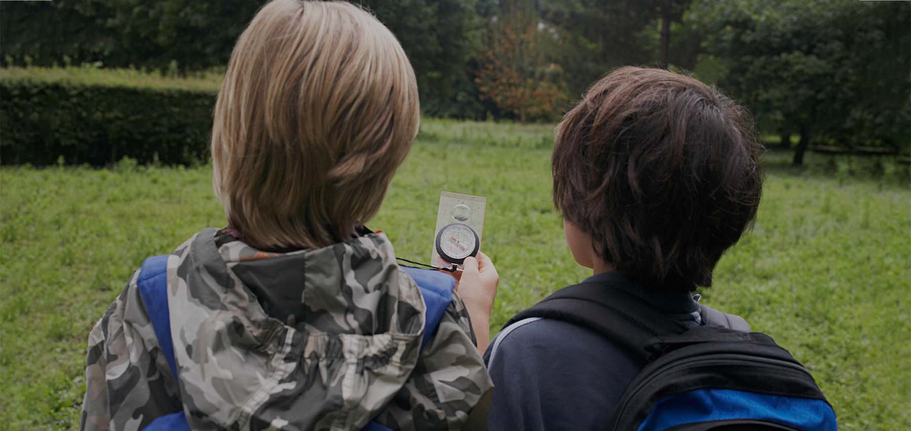 A photo from behind of two young boys looking at a compass whilst orienteering