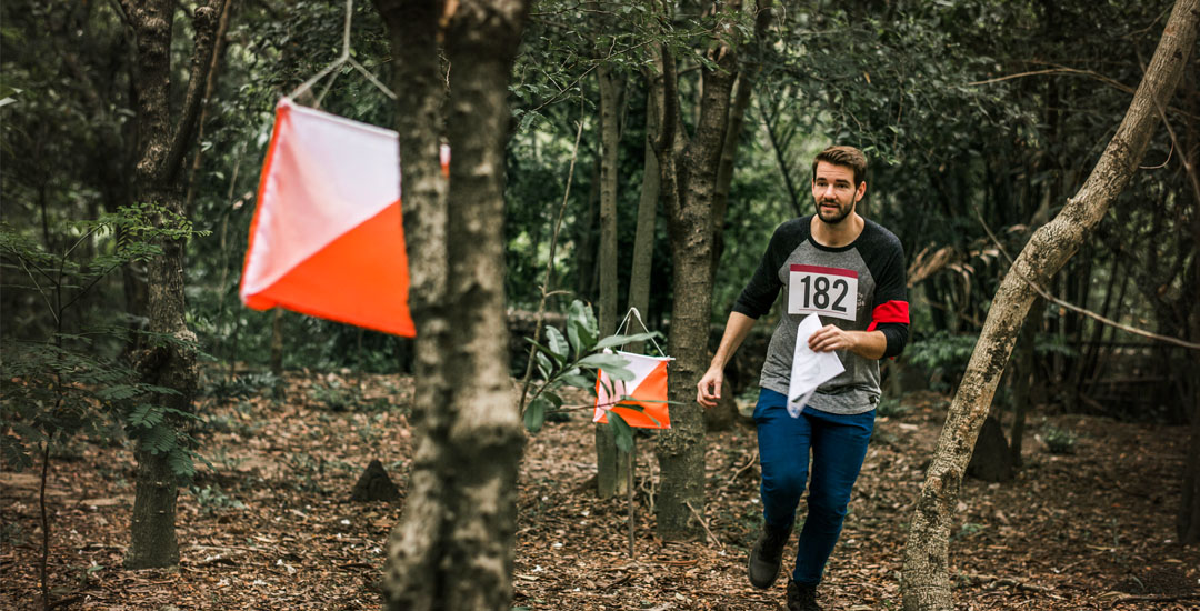 A man wearing a 182 number tag is orienteering in the forest