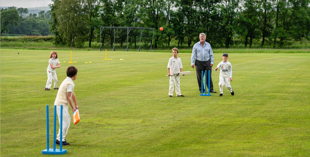 A man looks on as four children play cricket outdoor