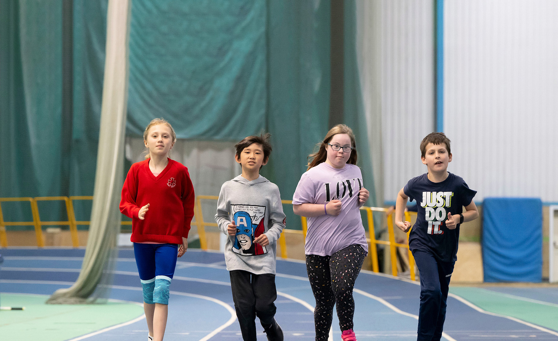 A group of four children run on an indoor race track