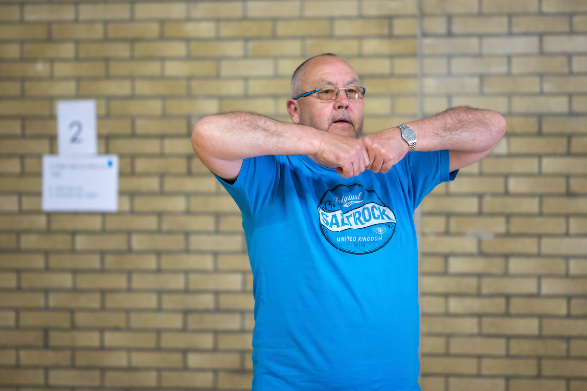A middled aged gentleman in a blue t-shirt works out in a sports hall
